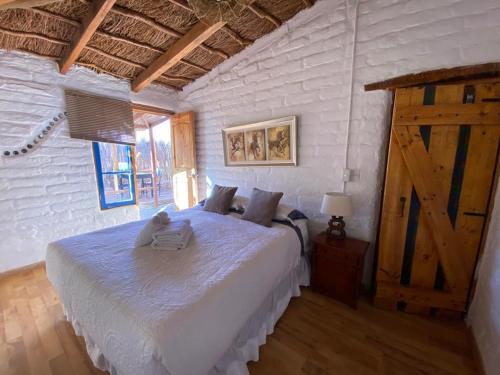 1 dormitorio con cama blanca y suelo de madera en Atacama Lodge Rukazen Spa Rústico, en San Pedro de Atacama