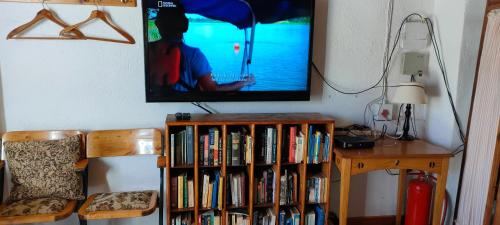 un televisor colgado en una pared con un estante lleno de libros en Den Hagen Guest Farm, en Rhodes