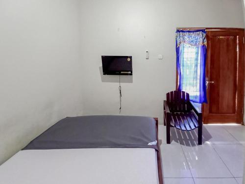 Schlafzimmer mit einem Bett, einem TV und einem Stuhl in der Unterkunft Hotel Gerung 2 near Luwes Mall Nganjuk Mitra RedDoorz in Nganjuk