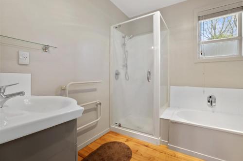 La salle de bains blanche est pourvue d'une douche et d'un lavabo. dans l'établissement Pukeko Lodge - Tūrangi Holiday Home, à Turangi