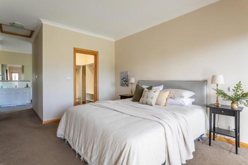 a white bedroom with a large bed and a mirror at Norfolk Bay Retreat - views over the sea and vines in Koonya