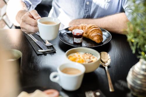 a table with a plate of food and cups of coffee at Le Marin Hotel Rotterdam City - Handwritten Collection in Rotterdam