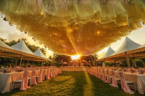 a group of tables and chairs in a field with the sun setting at Wanda Reign Resort & Villas Sanya Haitang Bay in Sanya