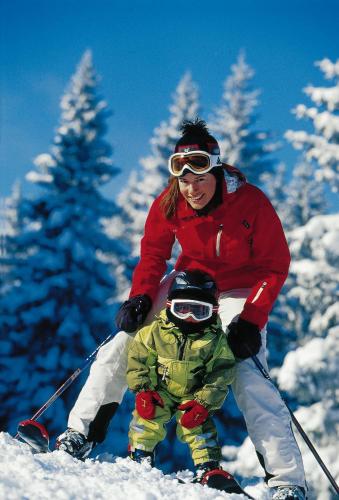 a woman and a child on skis in the snow at Hotel Bischofsmütze in Filzmoos