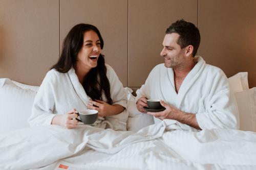 a man and a woman sitting in bed holding cups at Pan Pacific Perth in Perth