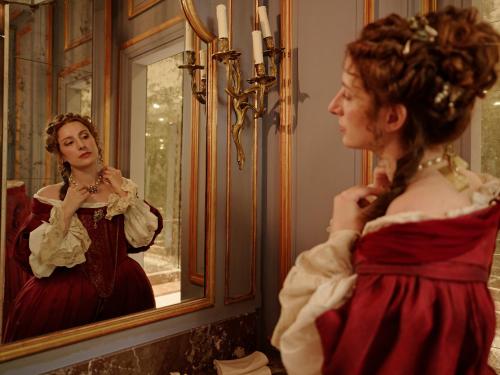 a woman in a red dress looking in a mirror at Relais & Château Louise de La Vallière in Reugny