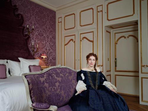 a woman sitting on a chair in a room with a bed at Relais & Château Louise de La Vallière in Reugny