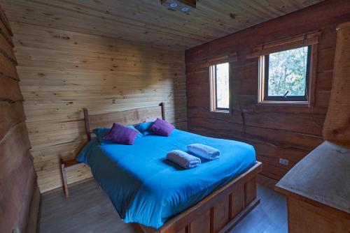 a bedroom with a blue bed in a wooden cabin at Entre Pampa y Bosque in Villarrica