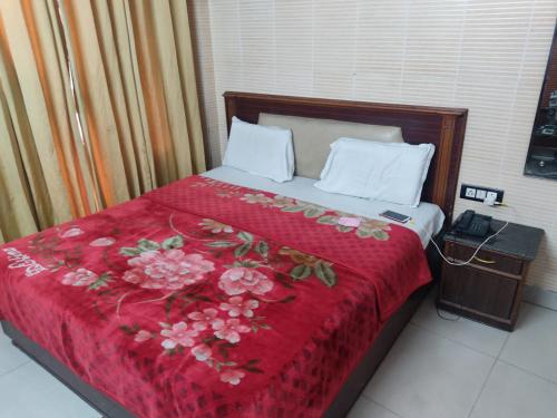 Una cama con una manta roja con flores. en Hotel Surya Excellency By WB Inn, en Jammu