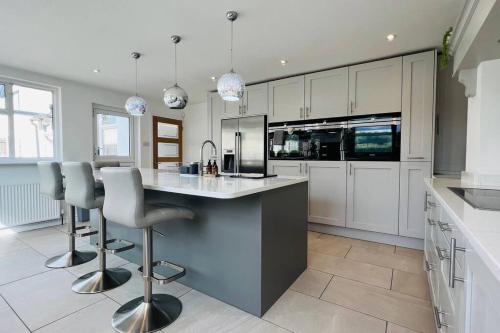 a kitchen with white cabinets and a island with bar stools at The Retreat Birchwood by Kasar Stays in Kent