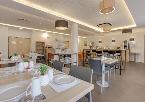 a dining room with tables and chairs and a kitchen at All Suites Appart Hôtel - Bordeaux - Pessac in Pessac