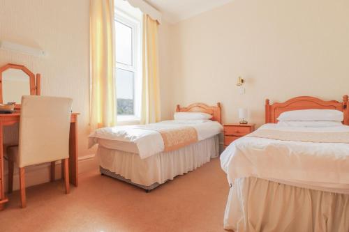 a bedroom with two beds and a desk and a window at Falcon's Nest Hotel in Port Erin