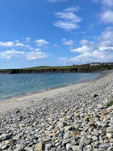 a rocky beach with the water and houses in the background at Modern self catering apartment, Miltown Malbay in Miltown Malbay