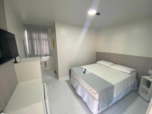 a white bedroom with a bed and a television at Veleiro Praia Hotel in Maceió