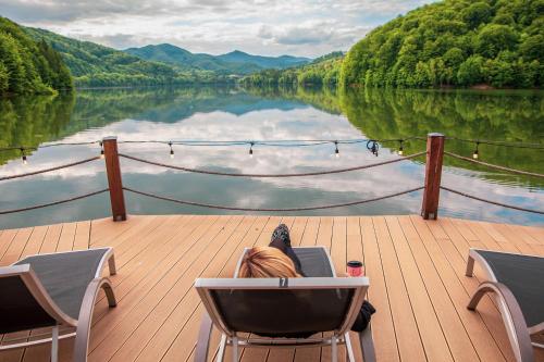 a woman laying in a chair on a wooden deck overlooking a lake at Adventure Lake Resort - Simared in Baia Mare