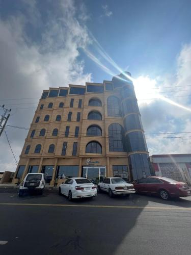 wysoki budynek z samochodami zaparkowanymi przed nim w obiekcie فندق التلال الخضراء w mieście An Nimāş
