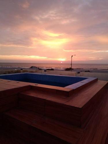 a swimming pool on the beach with the sunset in the background at Bungalow VerdeMar con Jacuzzi Frente al Mar in Vichayito