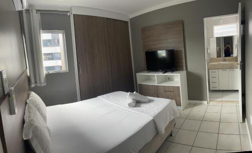 Schlafzimmer mit einem weißen Bett und einem TV in der Unterkunft Edifício Mariana Apto com 3 Quartos - Jatiúca in Maceió