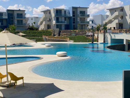 a swimming pool with chairs and an umbrella and some buildings at Fouka bay luxurious chalet in Marsa Matruh