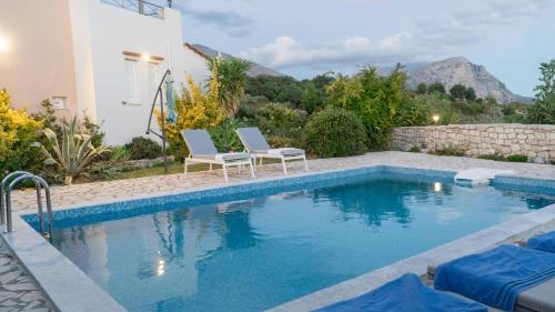 a swimming pool with two chairs next to a house at villa Nefeli in Lambiní