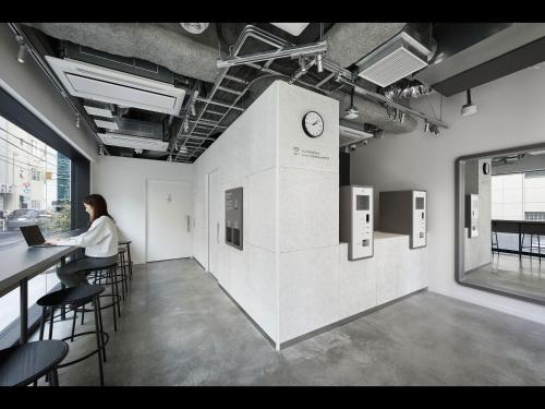 a woman sitting at a counter in an office with a clock on a wall at 9h nine hours Ningyocho in Tokyo