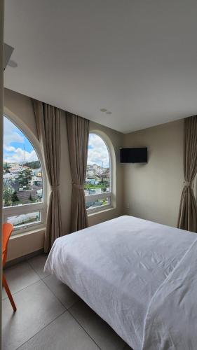 a bedroom with a large bed and two windows at Raon THT Hotel in Da Lat