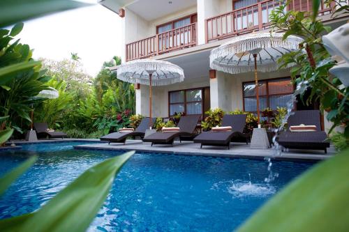 einen Pool mit Stühlen und Sonnenschirmen neben einem Gebäude in der Unterkunft Kayu Sugih Palace in Sanur