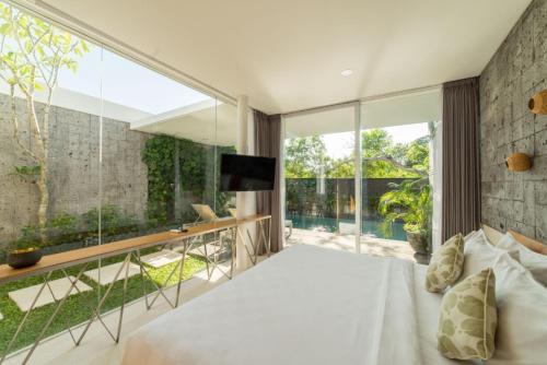 a bedroom with a white bed and a large window at Hideaway Villas Bali Uluwatu by Kanaan Hospitality in Uluwatu