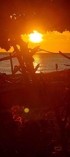 a sunset on the beach with a person in the water at Isin Gumi Homestay in Amed
