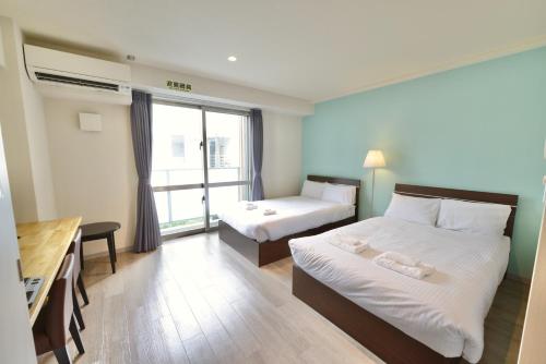 a bedroom with two beds and a desk and a window at Hotel2020 ホテル2020 in Kohagura