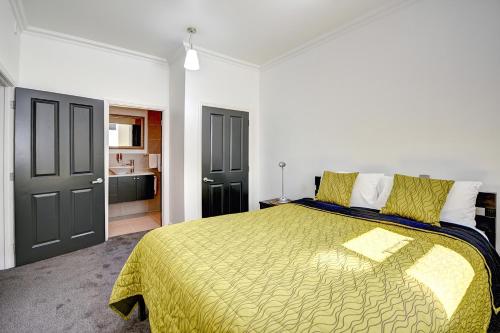 a bedroom with a large bed with a yellow blanket at Chapel Apartments in Dunedin