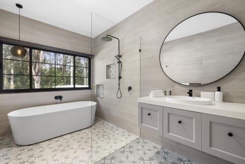 ein Badezimmer mit einer Badewanne, einem Waschbecken und einem Spiegel in der Unterkunft Koala Lane in Bonville