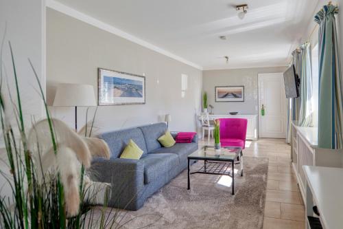 a living room with a blue couch and pink chairs at Fitschen am Dorfteich in Wenningstedt