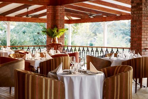 a restaurant with white tables and chairs and windows at Pioneers in Victoria Falls