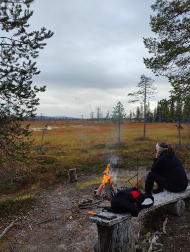 a man sitting on a bench next to a fire at Isokelo Log Apartments in Salla
