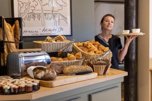a woman standing behind a counter with a tray of bread at Hotel Abbatial Saint Germain in Paris