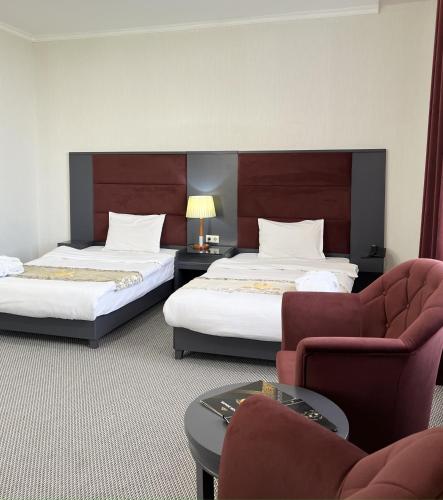 a hotel room with two beds and a chair at Almaty Grand Erbil Hotel in Almaty