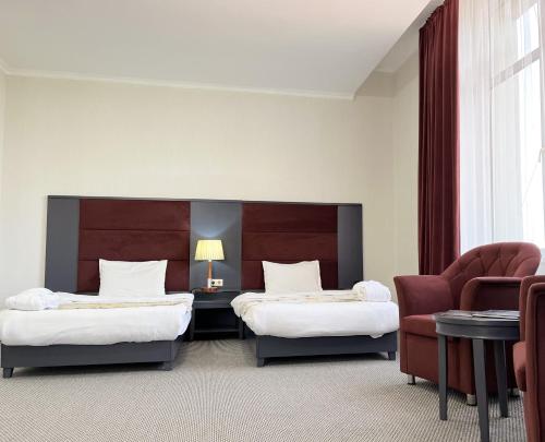 a hotel room with two beds and a chair at Almaty Grand Erbil Hotel in Almaty