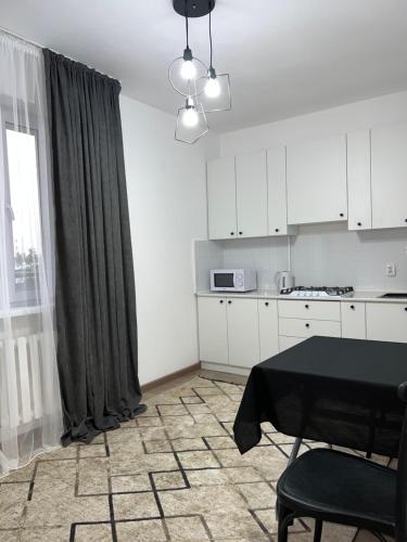 cocina con armarios blancos, mesa y ventana en Милая и уютная однокомнатная квартира в г.Тараз, en Taraz