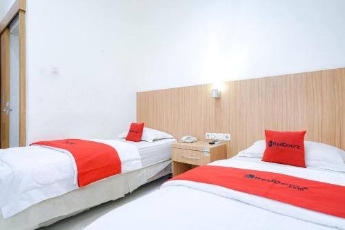 two beds in a hotel room with red and white at RedDoorz @ Avros Guest House Medan in Medan