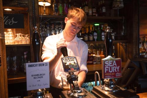 a man is standing behind a bar with a microphone at The Bamburgh Castle Inn - The Inn Collection Group in Seahouses