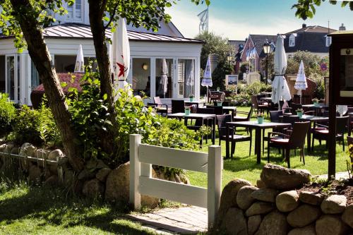 a white fence in front of a restaurant with tables and chairs at Fitschen am Dorfteich in Wenningstedt