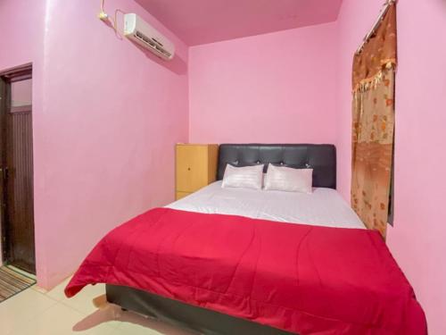 a bedroom with pink walls and a bed with a red blanket at Homestay Punokawan Puncak Indah Kota Malili Mitra RedDoorz in Malili