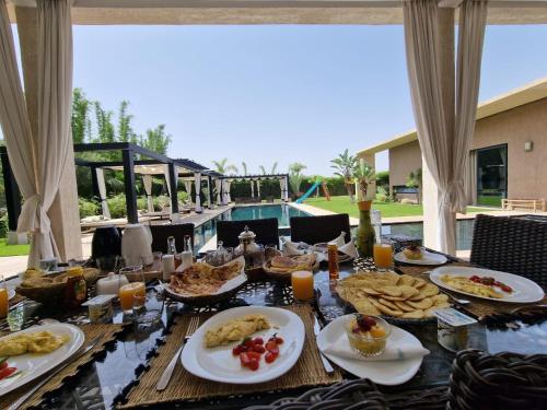 Villa Le Clos de l'Atlas في مراكش: طاولة مع أطباق من الطعام وحمام سباحة