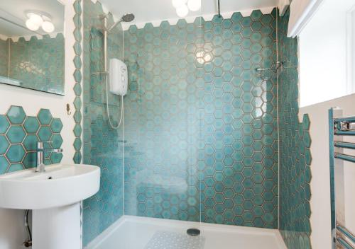 a bathroom with a blue tiled shower with a sink at Pineapple Cottage in Holt