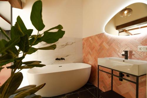 ein Badezimmer mit einer Badewanne, einem Waschbecken und einer Pflanze in der Unterkunft Logement In de Peel in Griendtsveen