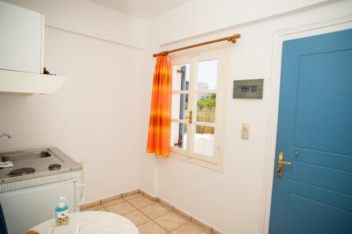 a kitchen with a blue door and a window at Manos Rooms in Megas Yialos-Nites