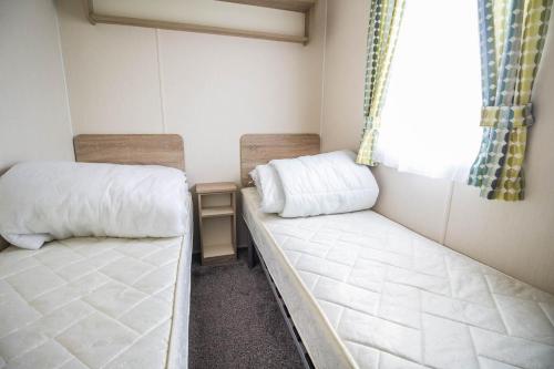 two beds in a small room with a window at Lovely Caravan With Decking At Seawick Holiday Park In Essex Ref 27471sw in Clacton-on-Sea