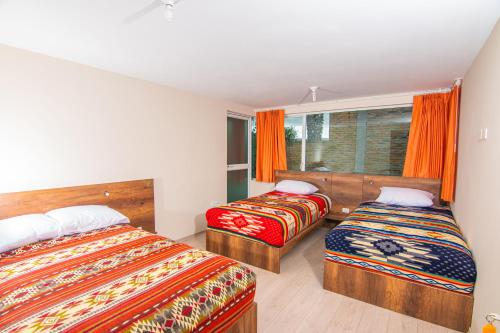 a bedroom with two beds and a window with orange curtains at The Traveler Hostel in Otavalo