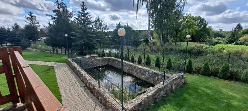a pond in a garden with a stone wall at Apartamenty Nad Stawem in Powidz